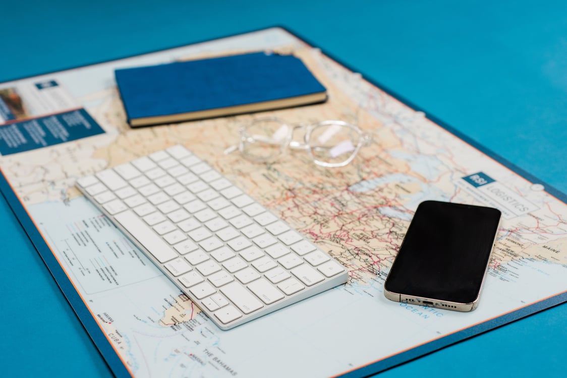 A blue notebook, black iphone, and white keyboard on a map of the rail networks of the united states